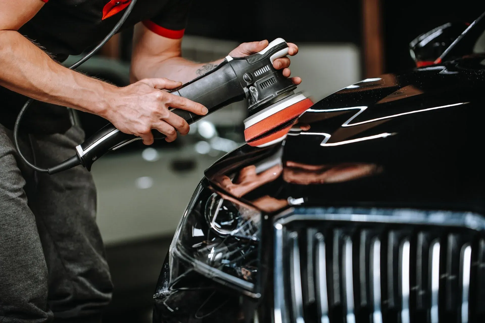 Person using orbital polisher on vehicle headlight during detailing service