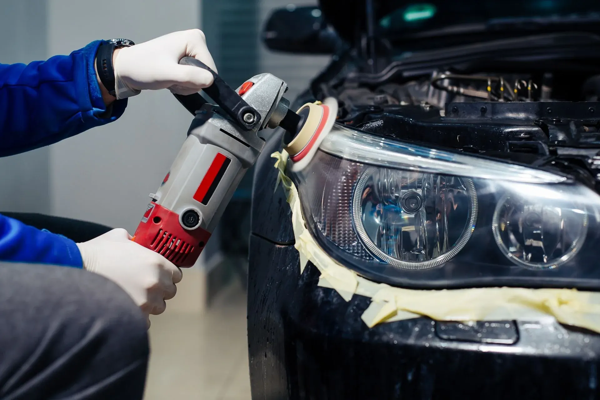 Professional detailer polishing car headlight with orbital buffer tool